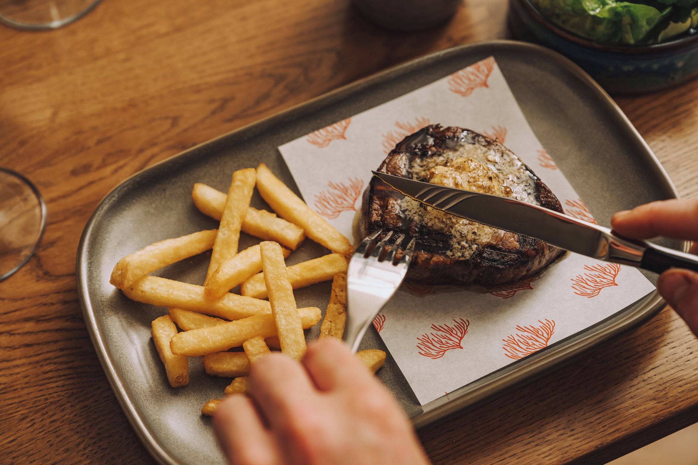 A plate with a steak and fries on a wooden table.