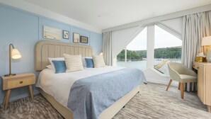 Una habitación de hotel con una cama grande, vista al agua, un escritorio y una silla.