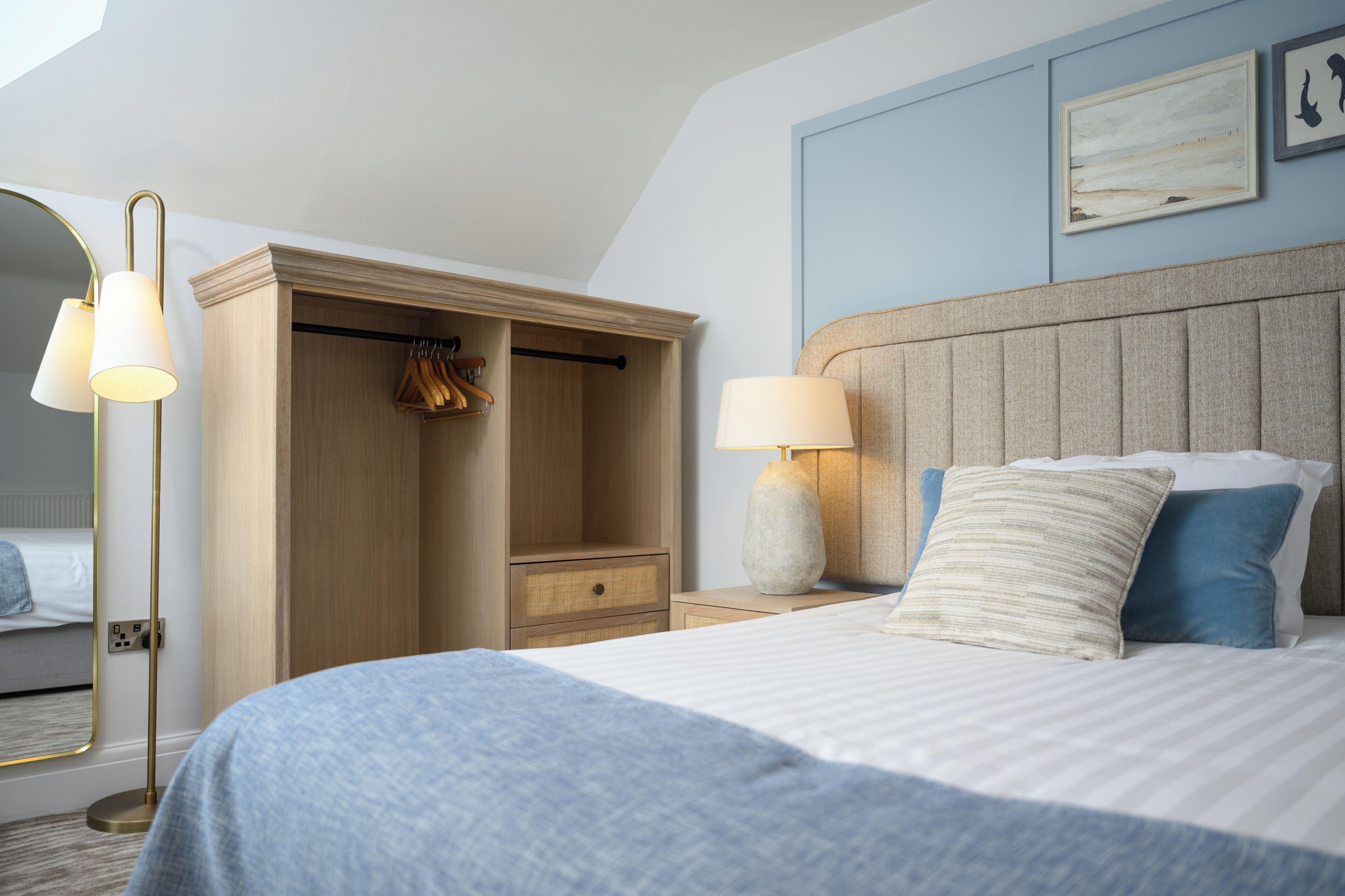 Une chambre d’hôtel avec un grand lit, une armoire, une table de chevet avec une lampe et un miroir.