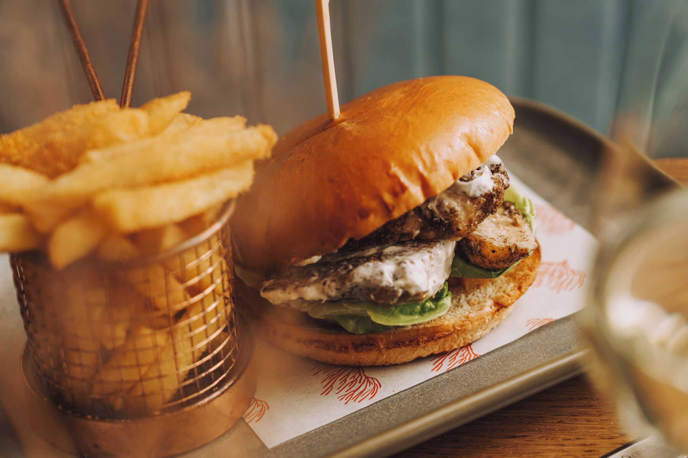 A burger with a bun, lettuce, and a piece of meat, accompanied by a basket of fries.