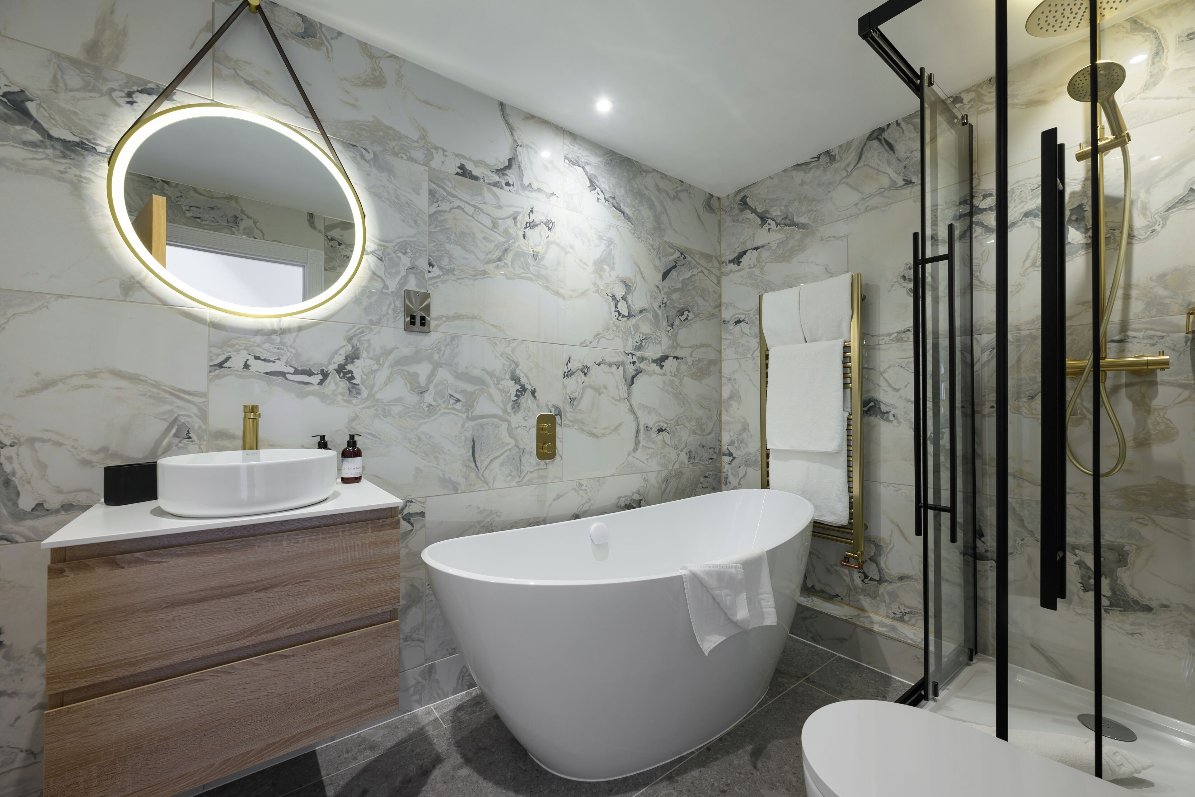 Ein modernes Badezimmer mit einer freistehenden Badewanne, einem runden Spiegel mit Beleuchtung und einer gläsernen Dusche.