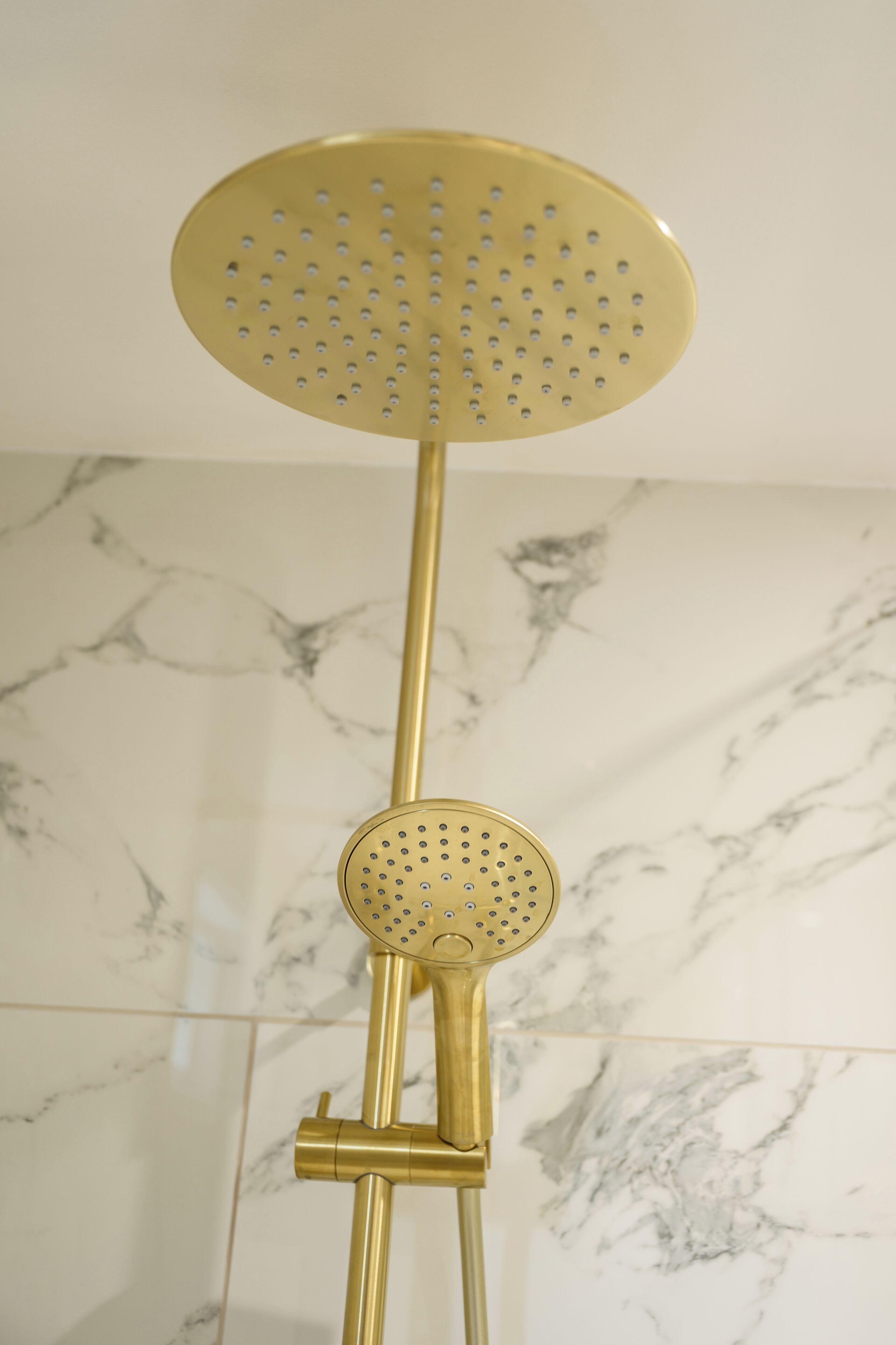 Un pommeau de douche de couleur dorée, doté d’une partie supérieure circulaire et d’une petite pièce circulaire fixée en dessous, le tout monté sur un support.