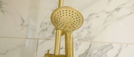 Un pommeau de douche de couleur dorée, doté d’une partie supérieure circulaire et d’une petite pièce circulaire fixée en dessous, le tout monté sur un support.
