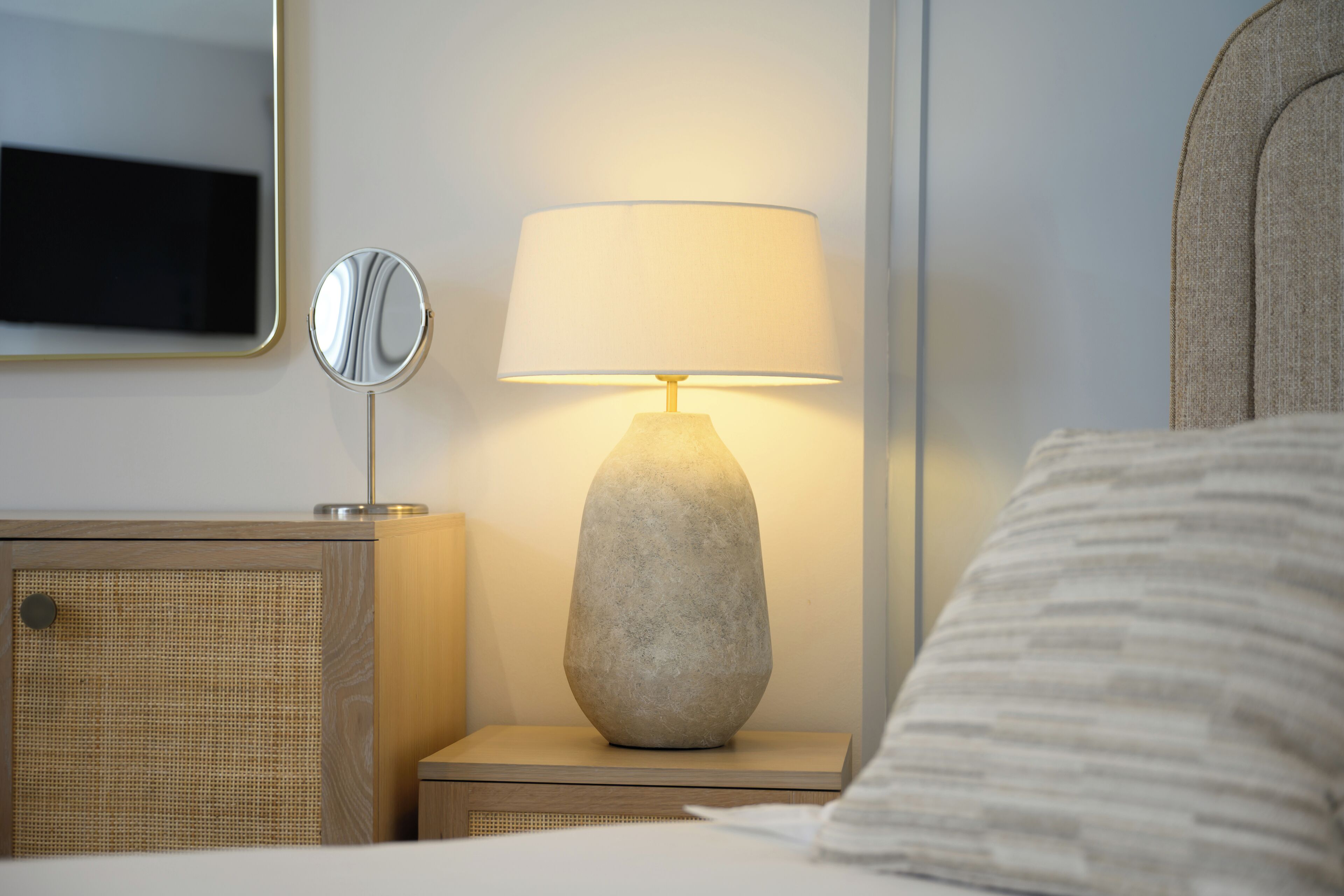 Una habitación de hotel ordenada con una cama, una lámpara de noche, un espejo y una mesita de noche de madera.