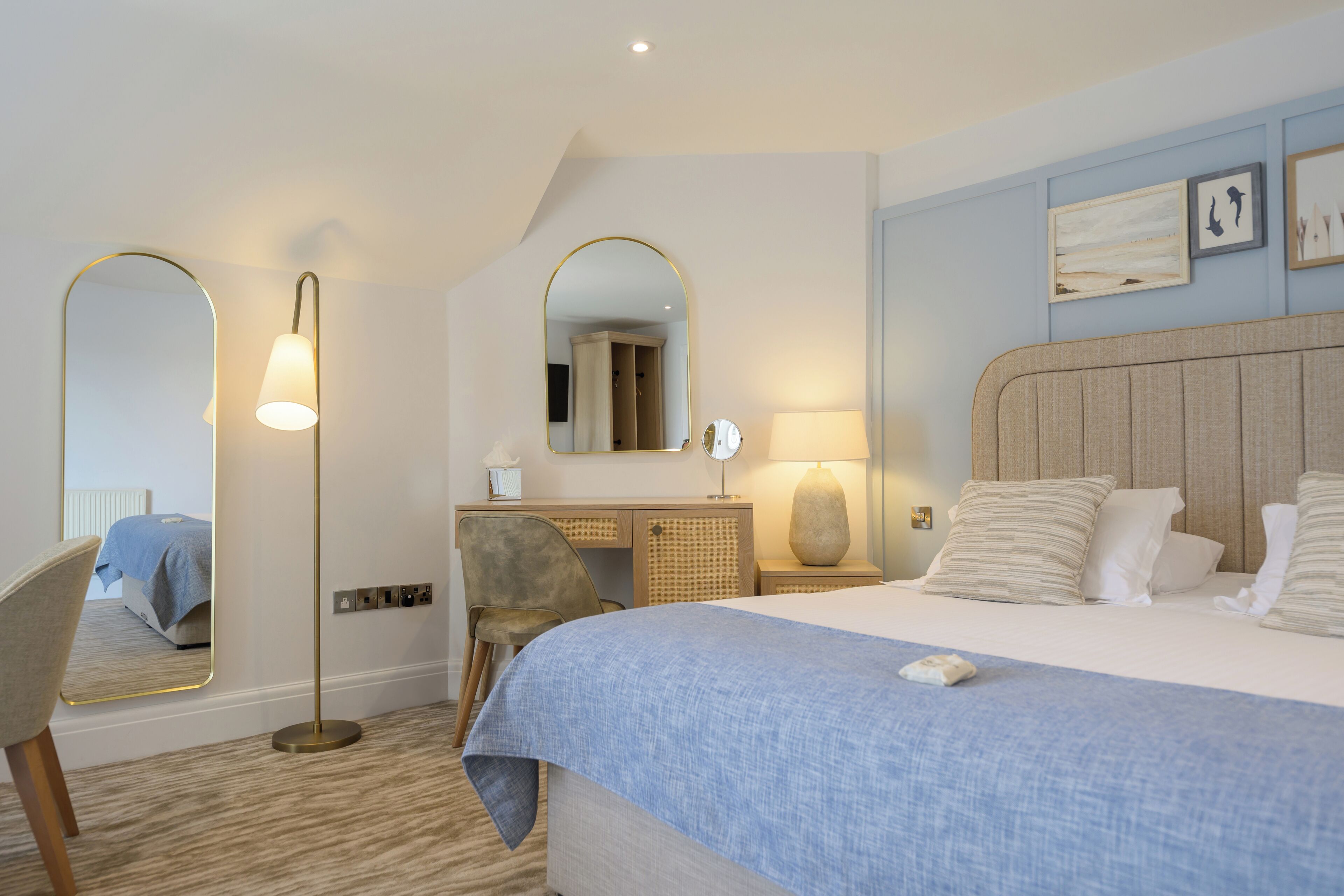 Una habitación de hotel con cama, escritorio, silla, espejo grande y lámpara.