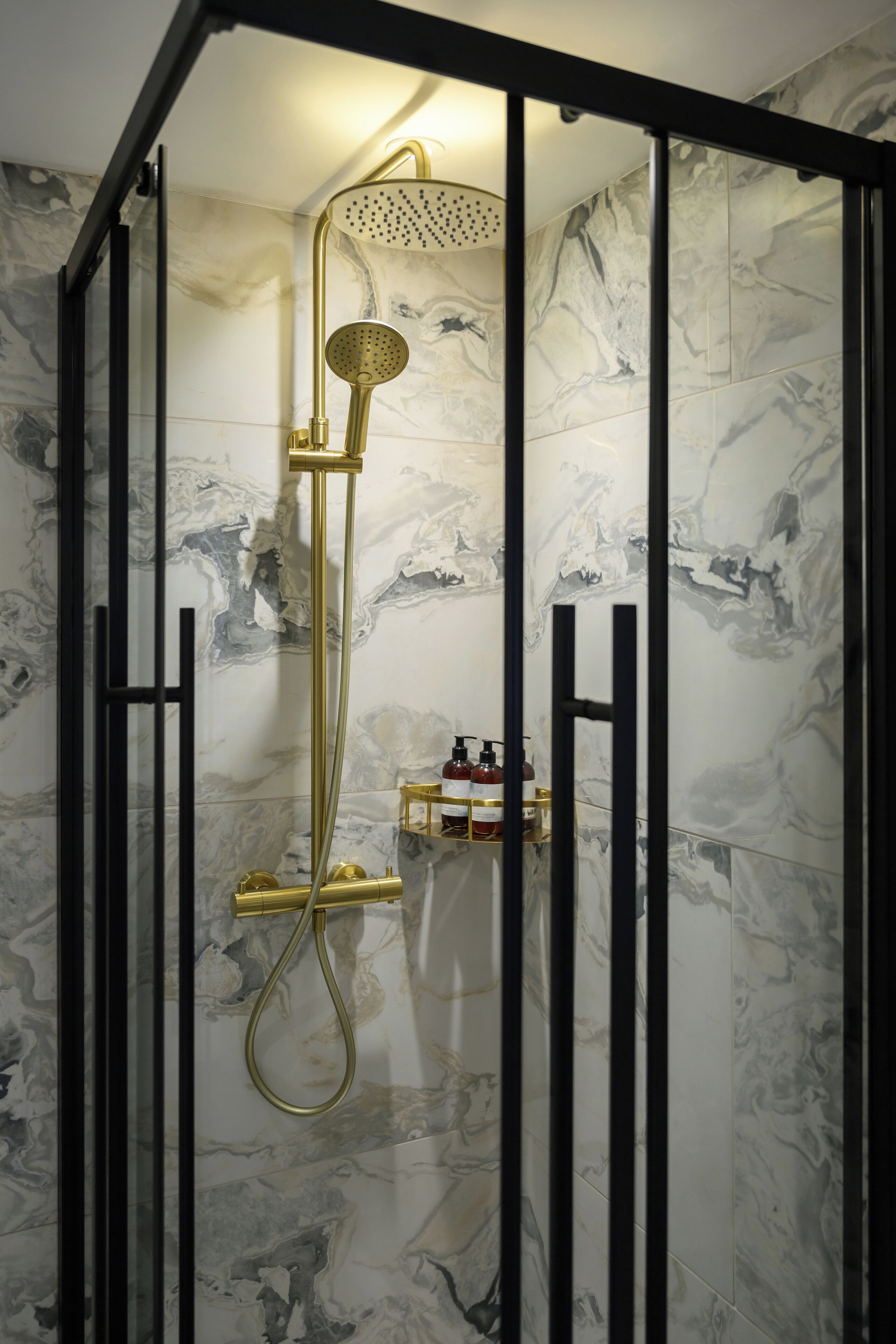 A shower with a gold fixture, marble walls, and a black frame.