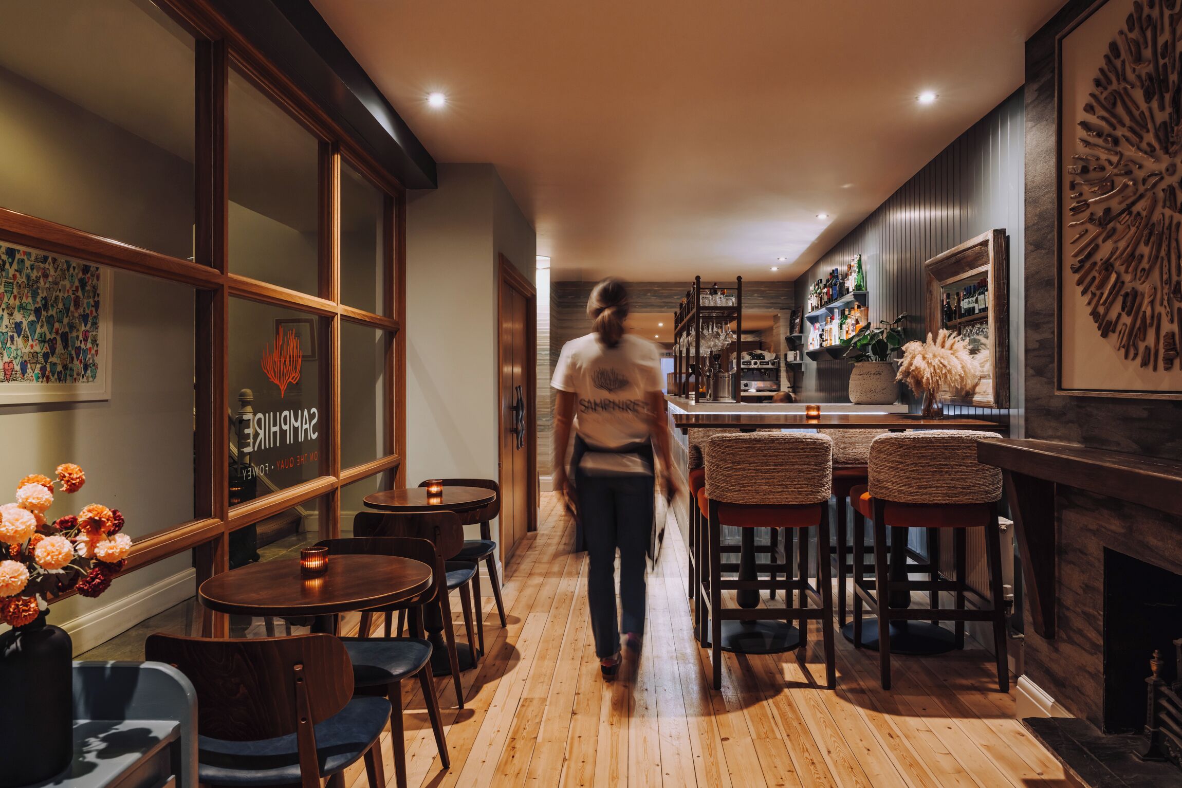 A modern interior with a wooden floor, bar area with stools, and a fireplace.