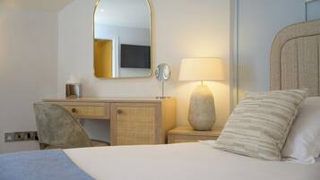 A hotel room with a bed, a desk with a mirror, a lamp, and a chair.