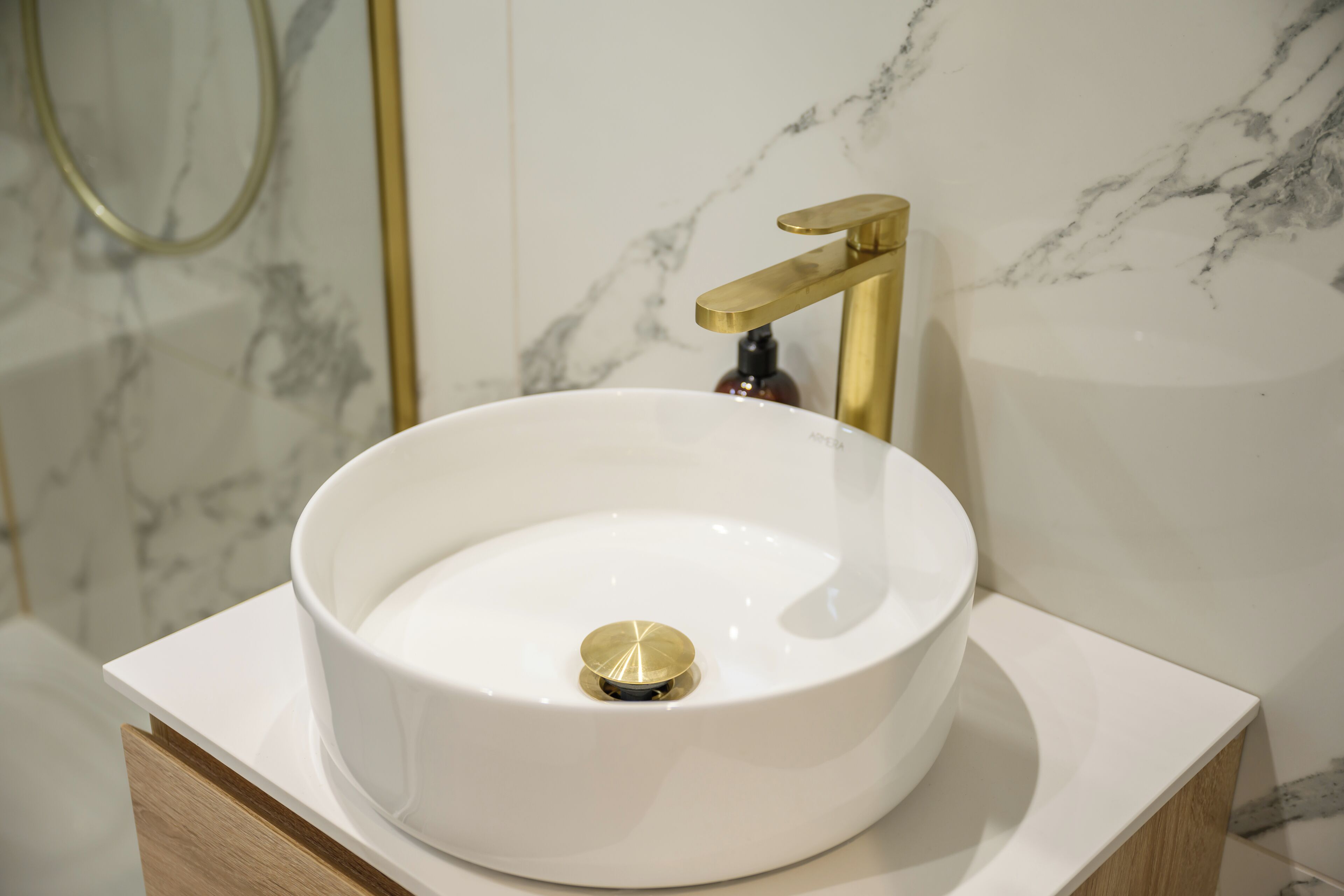 Une salle de bain avec un lavabo en marbre blanc, un robinet doré et un meuble en bois.