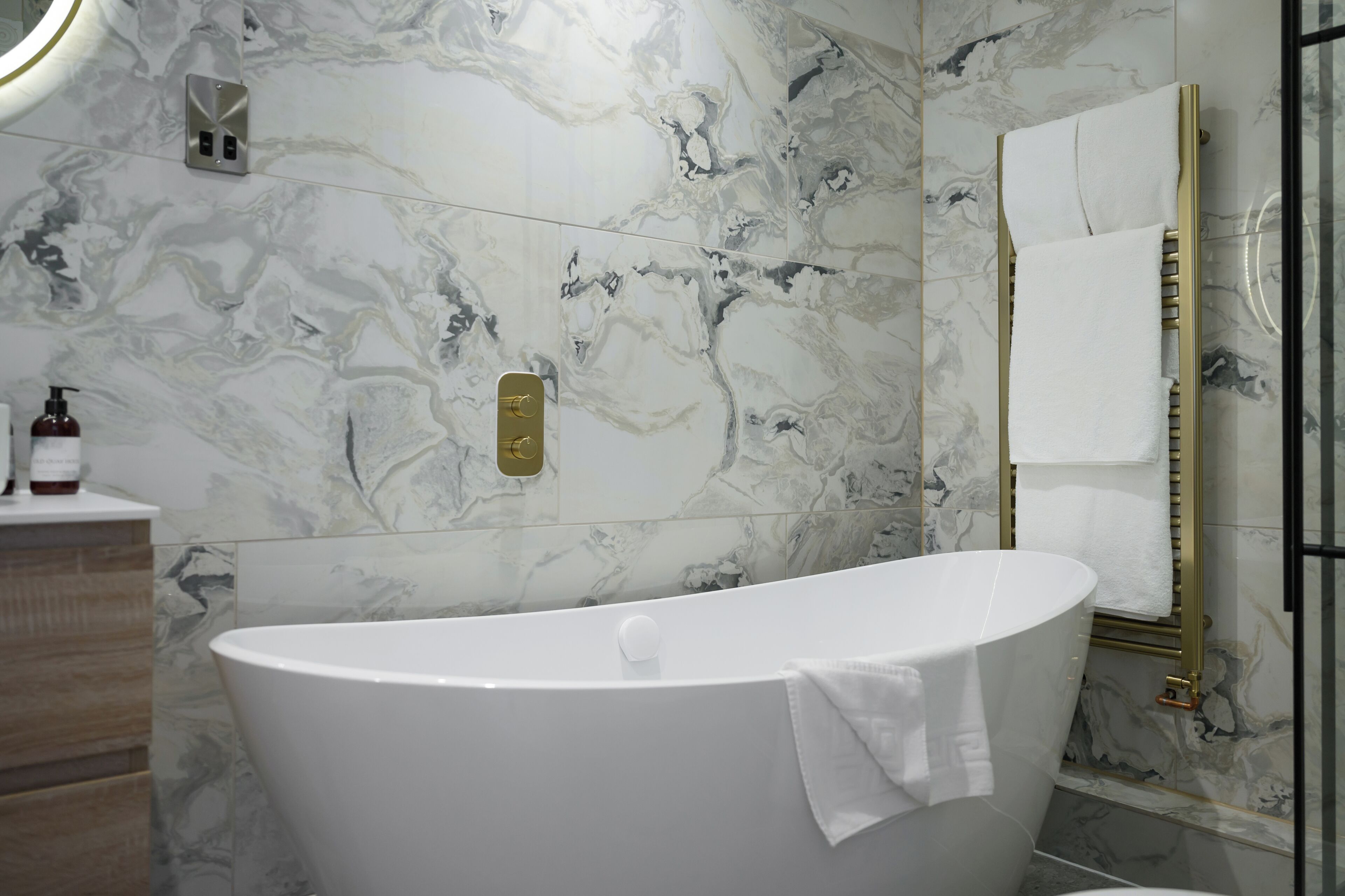 Ein modernes Badezimmer mit freistehender Badewanne, Marmorwänden und einem spiegel mit goldener Rahmung.