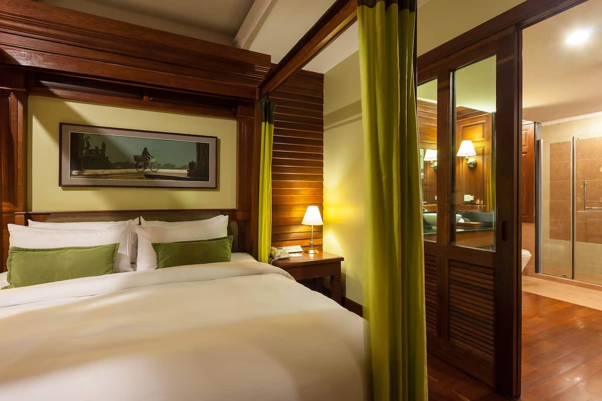 Una camera d'albergo con un letto grande, un comodino con una lampada, un quadro incorniciato appeso al muro e una porta scorrevole che dà su un bagno.