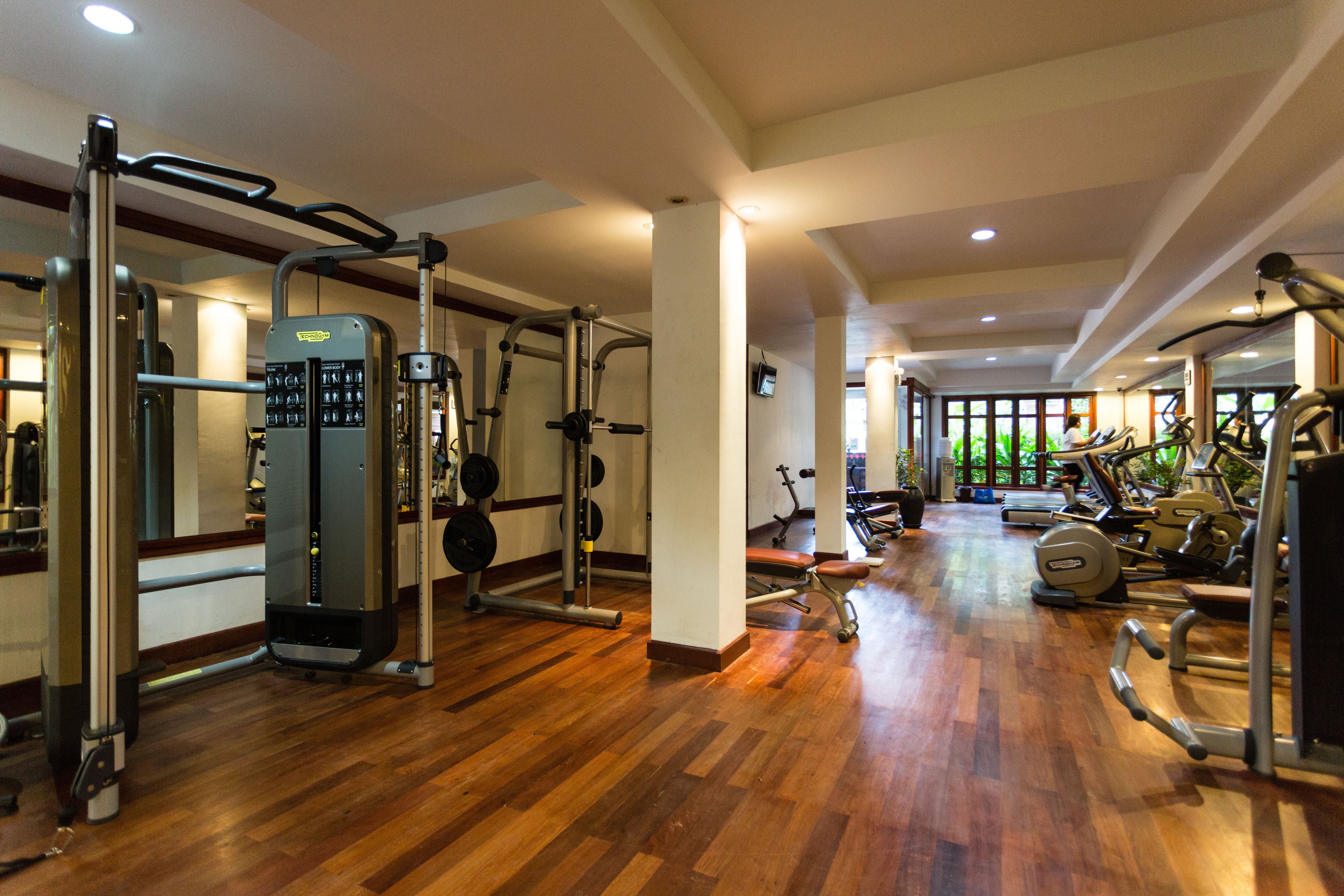 Ein Fitnessstudio mit unterschiedlichen Trainingsgeräten, Holzböden und großen Fenstern, die für natürliches Licht sorgen.