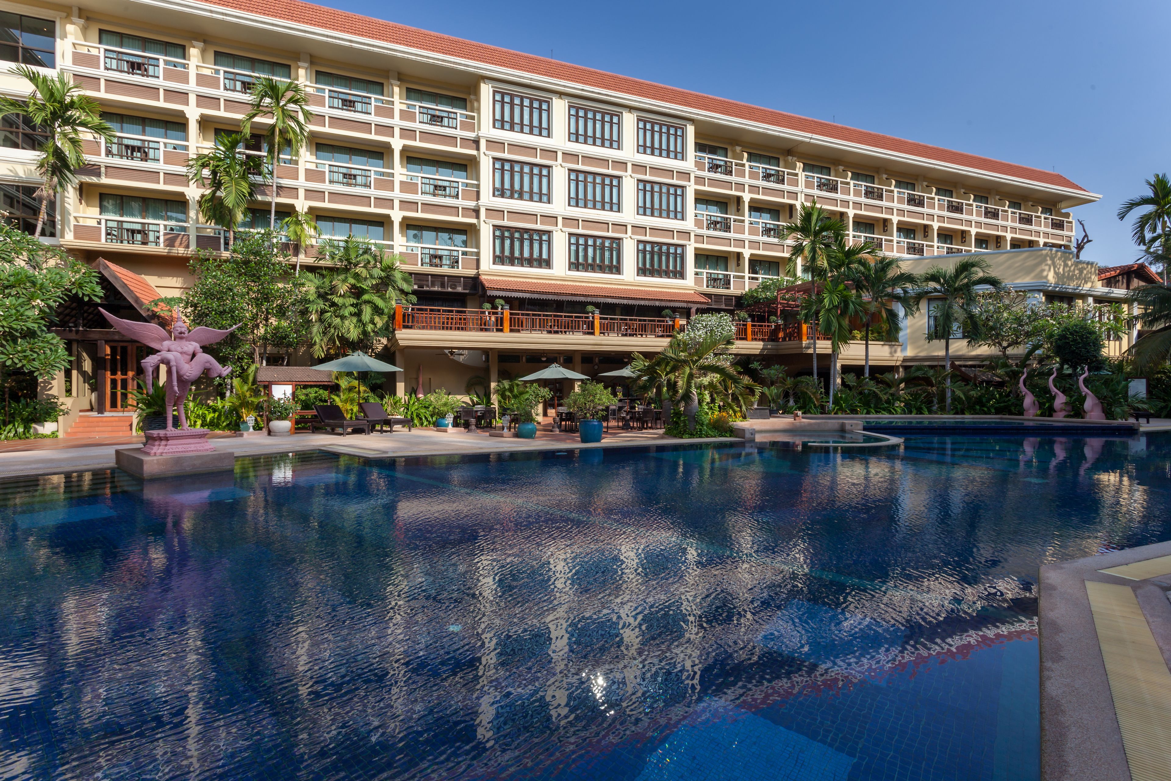 Ein Hotel mit großem Pool, Palmen und einem mehrstöckigen Gebäude mit Balkonen.