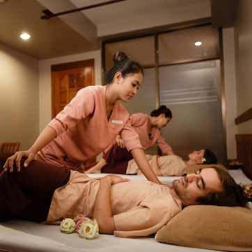 A massage therapy room with a massage table, a massage therapist, and a client receiving a back massage.