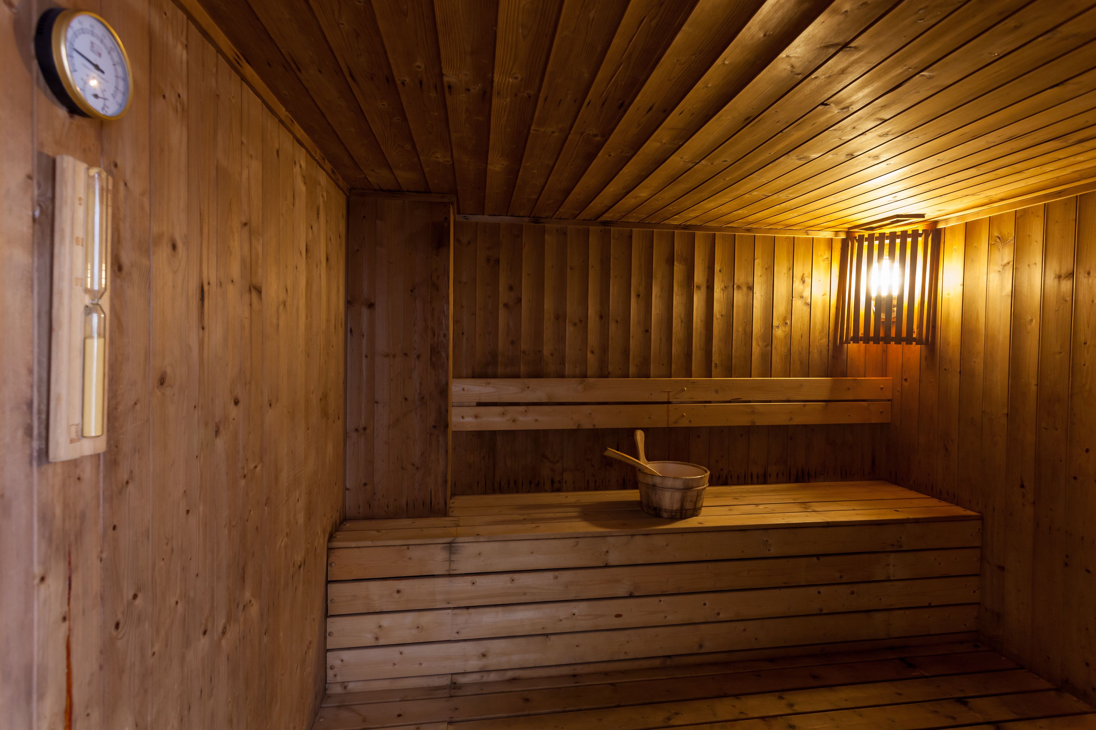Un sauna en bois avec des bancs, un thermomètre fixé au mur et un luminaire.