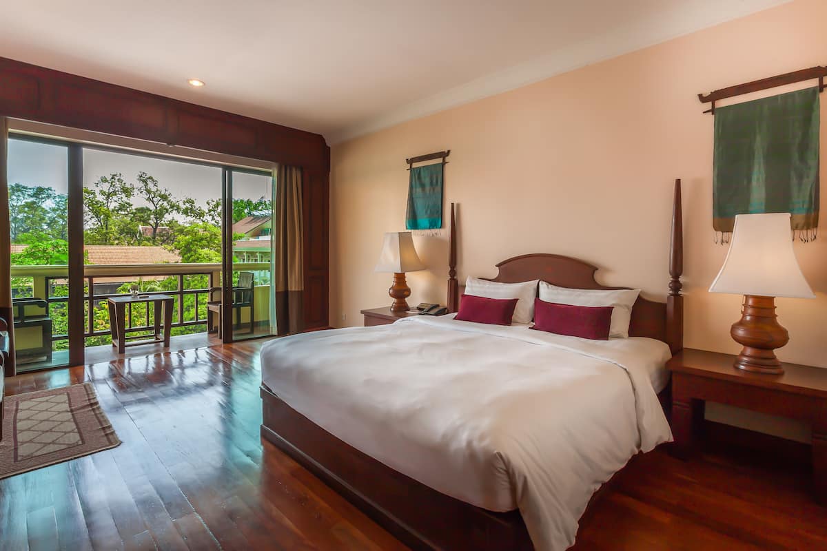 Un'ampia camera da letto con un letto grande, un comodino con una lampada, una testiera in legno e vista su un balcone con tavolo e sedie.