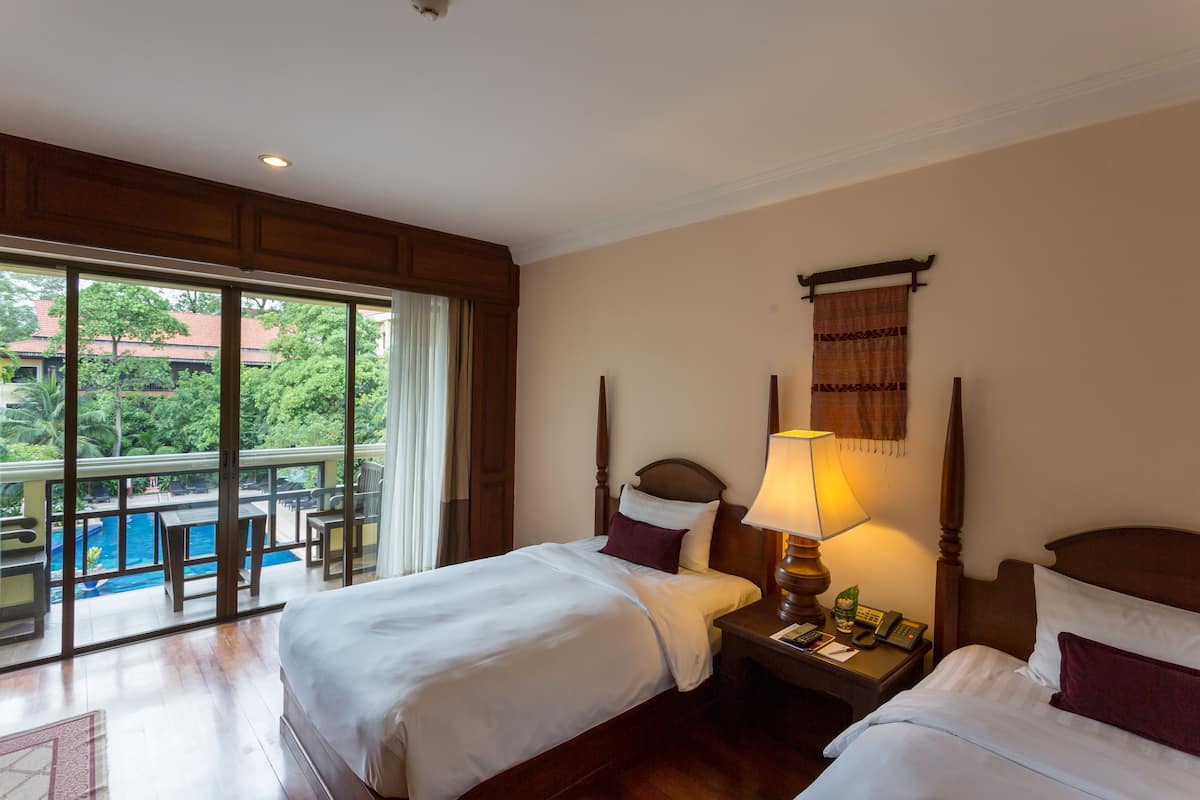 Una camera d'albergo con due letti, un balcone con piscina e vista sul verde.