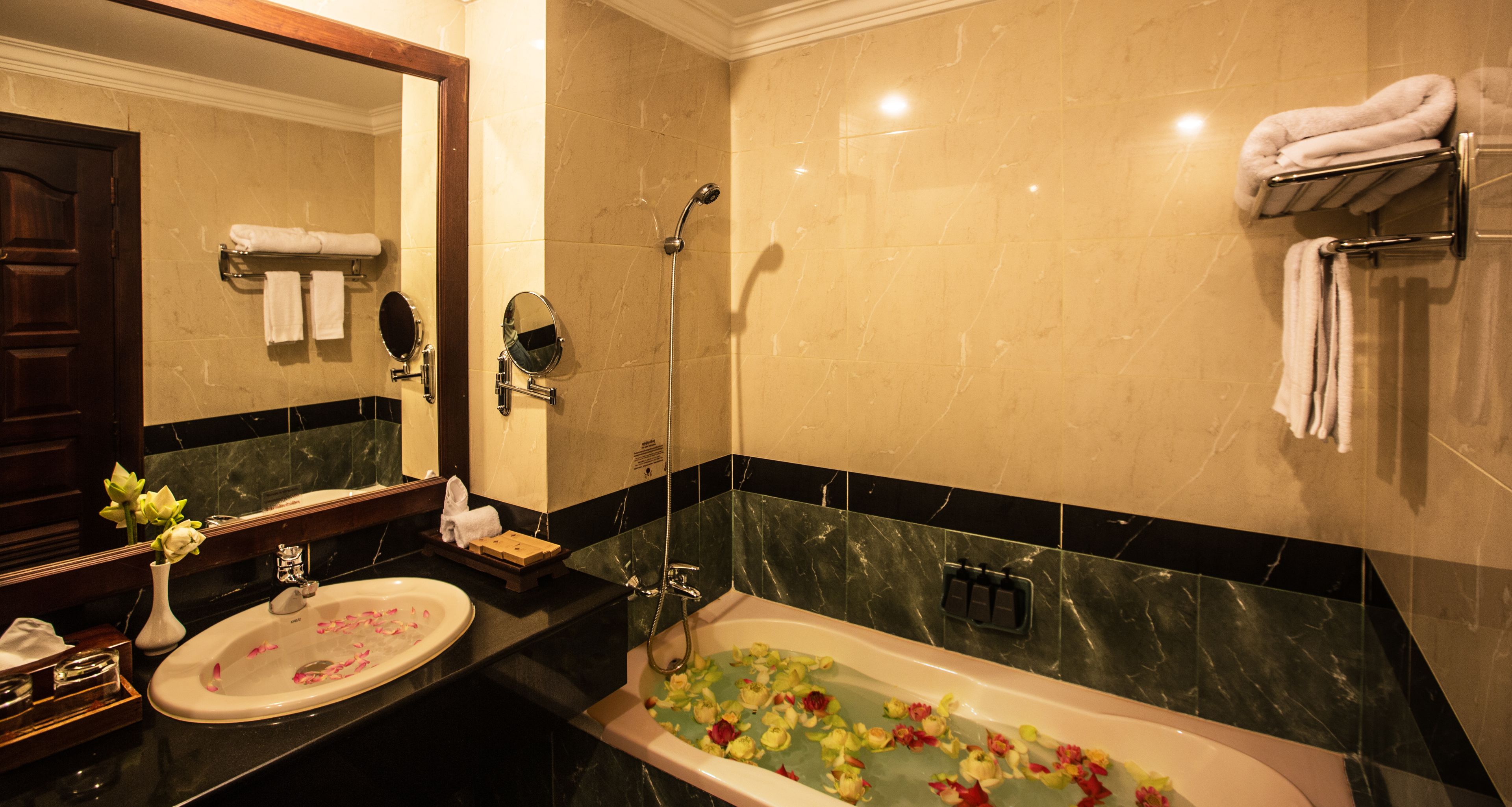 A bathroom with a bathtub filled with flowers, a sink, a mirror, and towels on a rack.