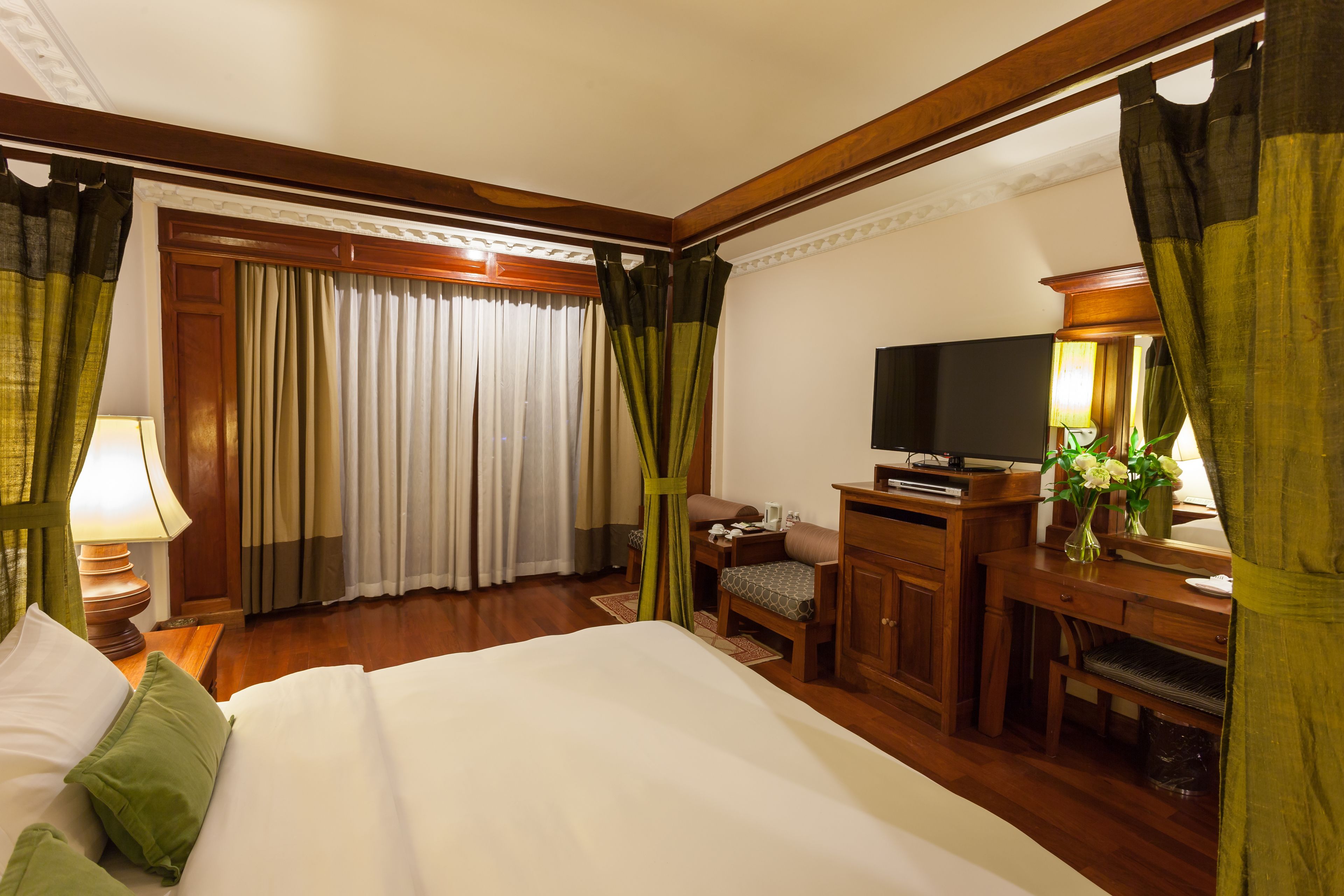 Una habitación de hotel con una cama grande, un escritorio con televisor, una silla y una lámpara de escritorio.