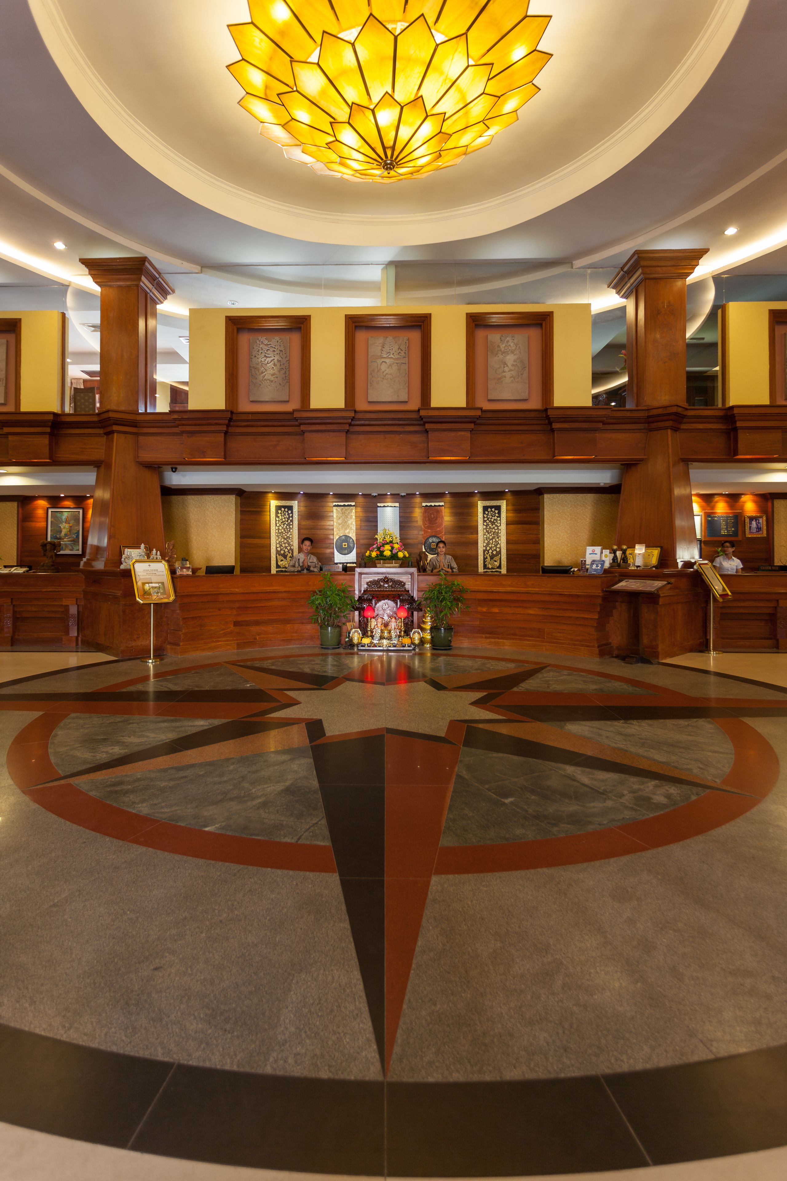 A hotel lobby with a central reception desk, a large chandelier, and a decorative fountain.