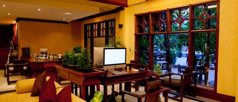 A well-lit indoor space with a computer desk, a sofa with patterned cushions, and a view of the outdoors through large windows.