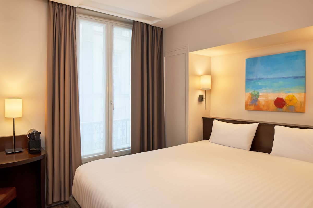 Una camera d'albergo con un letto grande, una scrivania con una lampada e un quadro raffigurante una spiaggia.