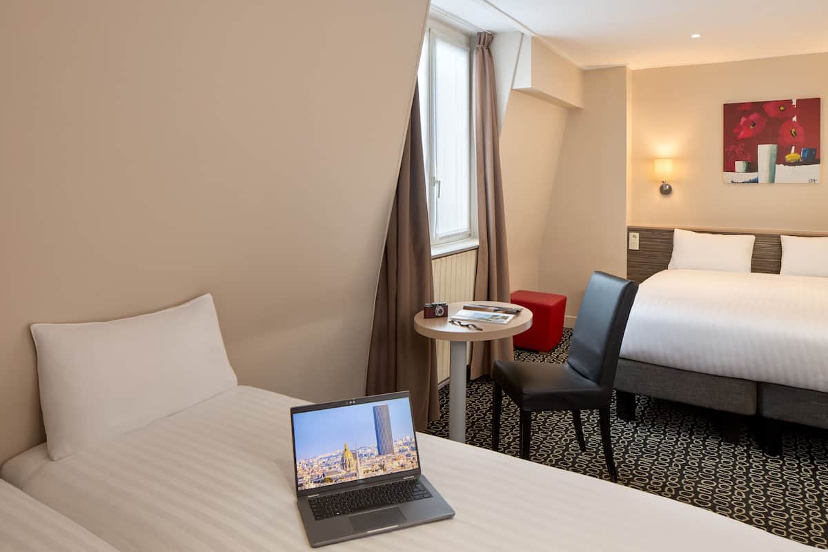 Una camera d'albergo con un letto, un portatile sul letto, un tavolino con una fotocamera e una sedia.