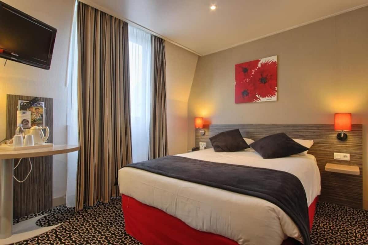 Una camera d'albergo con un letto, lampade sui comodini, una televisione, un tavolo con un vassoio e una finestra con tende.