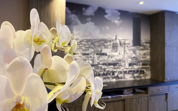 A close-up of white orchids with a cityscape mural in the background. - Timhotel Odessa Montparnasse (Paris)