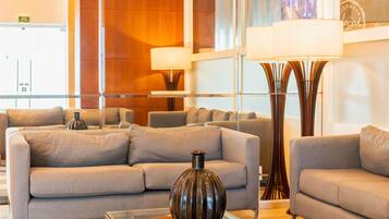 A modern hotel lobby with sofas, a glass coffee table, and floor lamps.