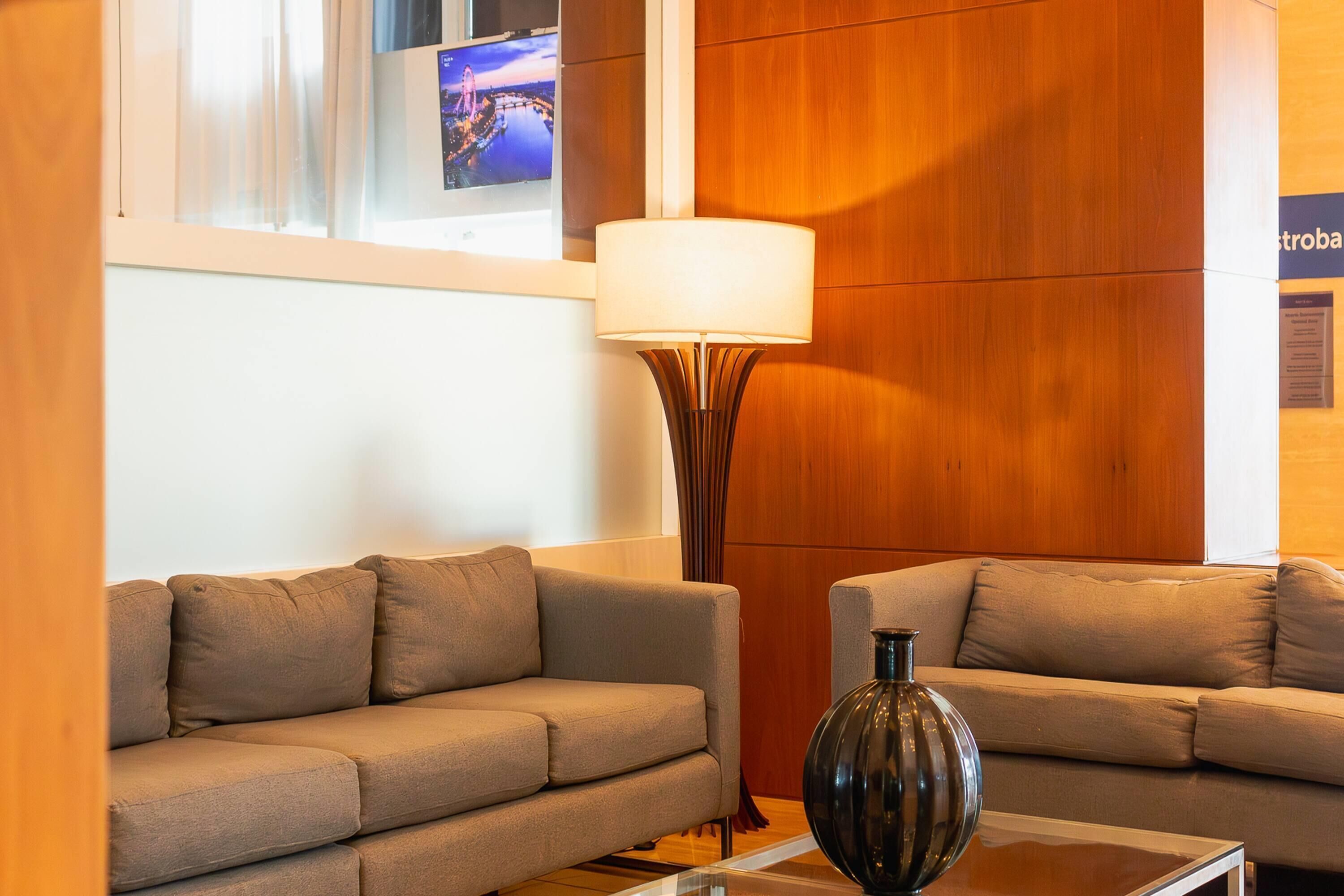 Una habitación de hotel moderna con dos sofás, una lámpara de pie y un televisor montado en la pared.