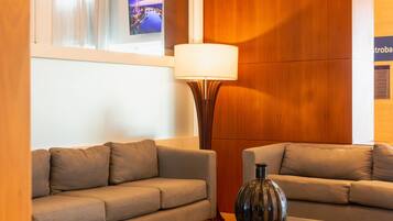 Una habitación de hotel moderna con dos sofás, una lámpara de pie y un televisor montado en la pared.