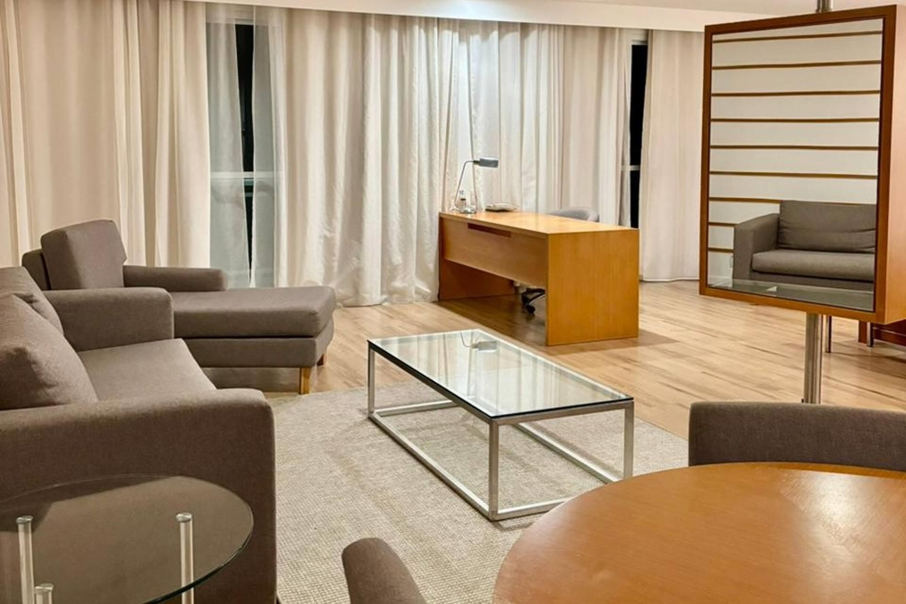 A modern living room with a sofa, a glass coffee table, a wooden desk, and a chair.