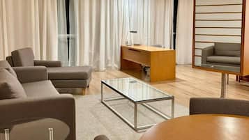 A modern living room with a sofa, a glass coffee table, a wooden desk, and a chair.
