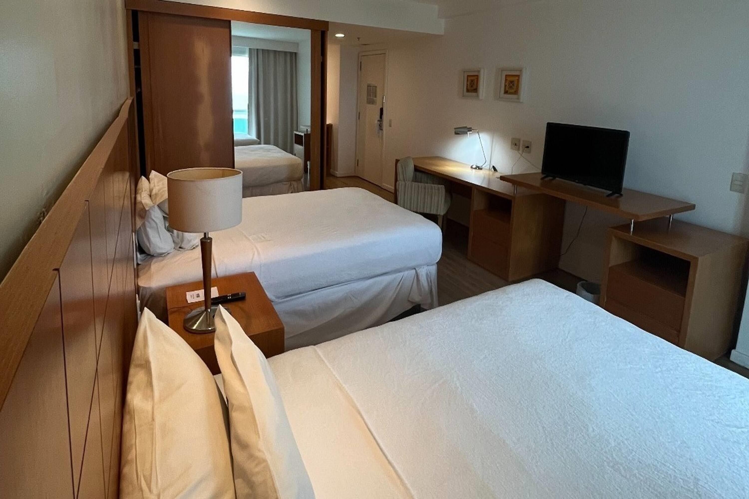 Une chambre d’hôtel avec deux lits, un bureau, une télévision et une lampe.