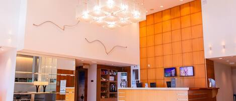 A modern hotel lobby with a reception desk, a seating area, and a large wooden wall.