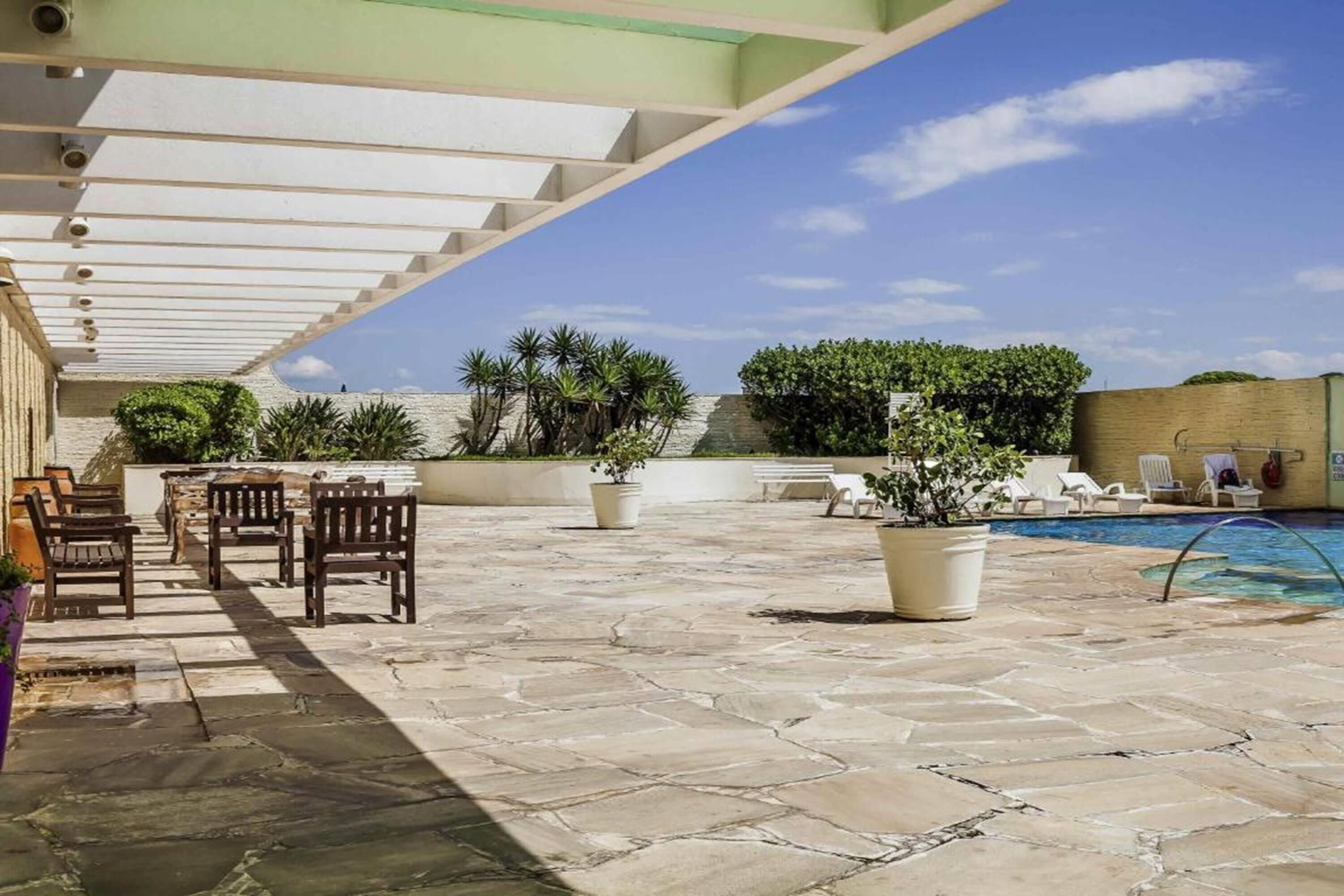 Un patio exterior con suelo de piedra, mobiliario, piscina y plantas en macetas.