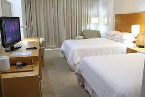 Een hotelkamer met twee bedden, een bureau met een computer, een stoel en een televisie.