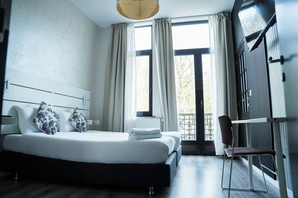 A modern hotel room with a large bed, a chair, and a view of the outside.