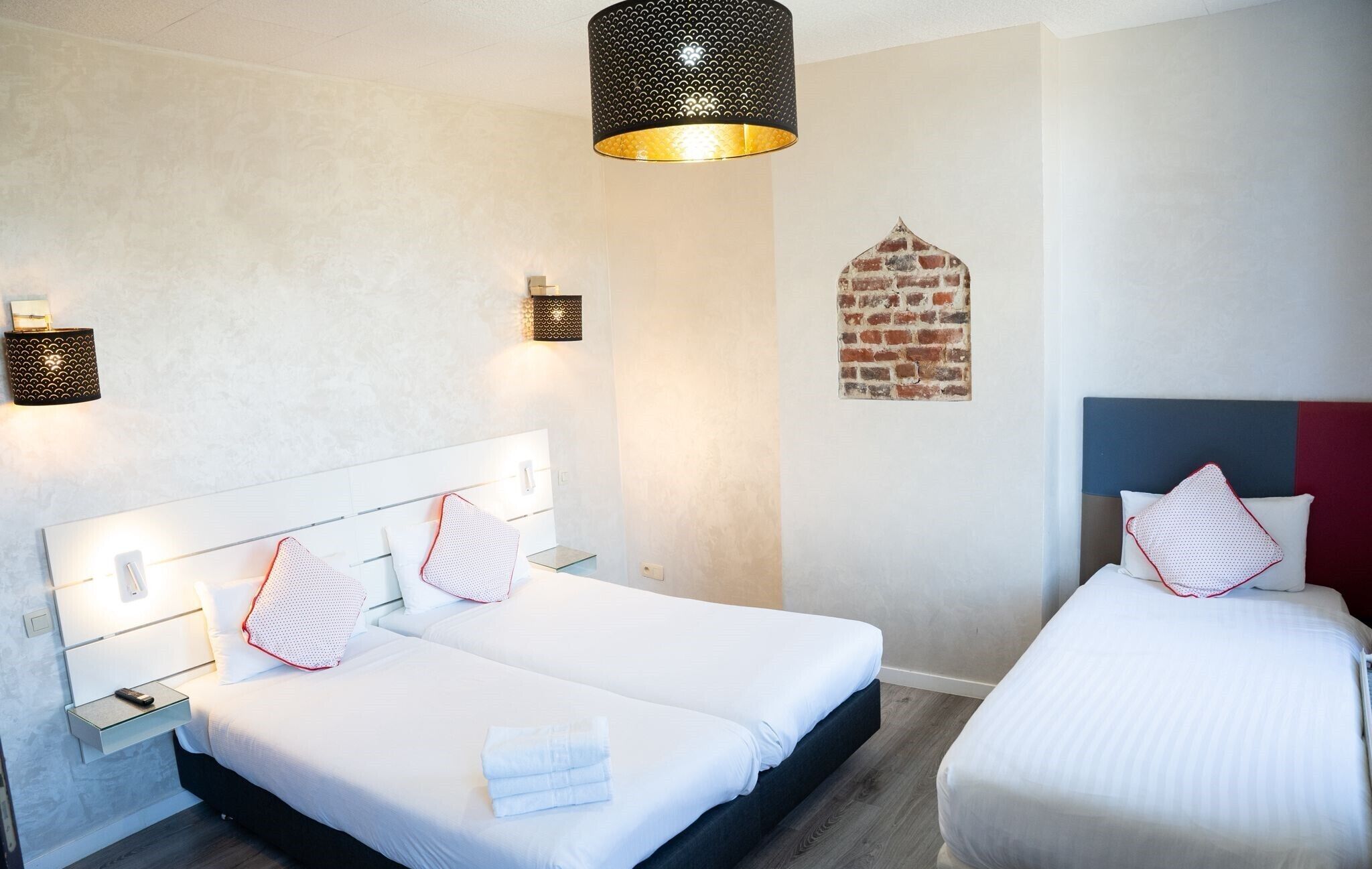 A hotel room with two beds, a brick wall decoration, and a modern light fixture.