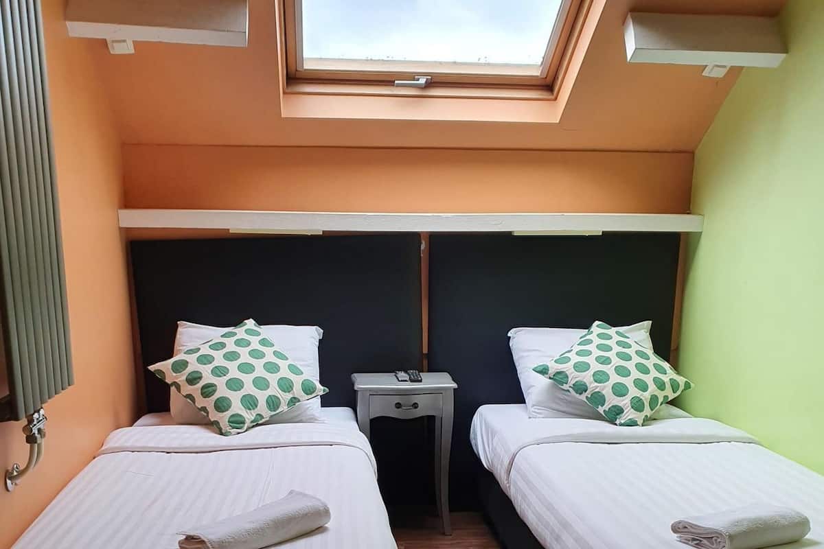 A room with two beds, a skylight, a small bedside table, and a green wall.