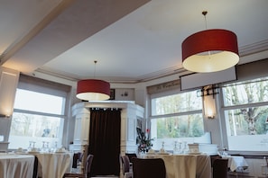 A dining area with tables set for service, large windows, and a red pendant light.