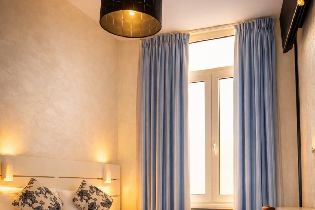 A modern hotel room with a large bed, bedside lamps, a desk, and a window with curtains.