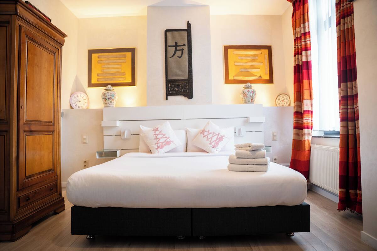 A bedroom with a large bed, wooden wardrobe, and decorative wall pieces.