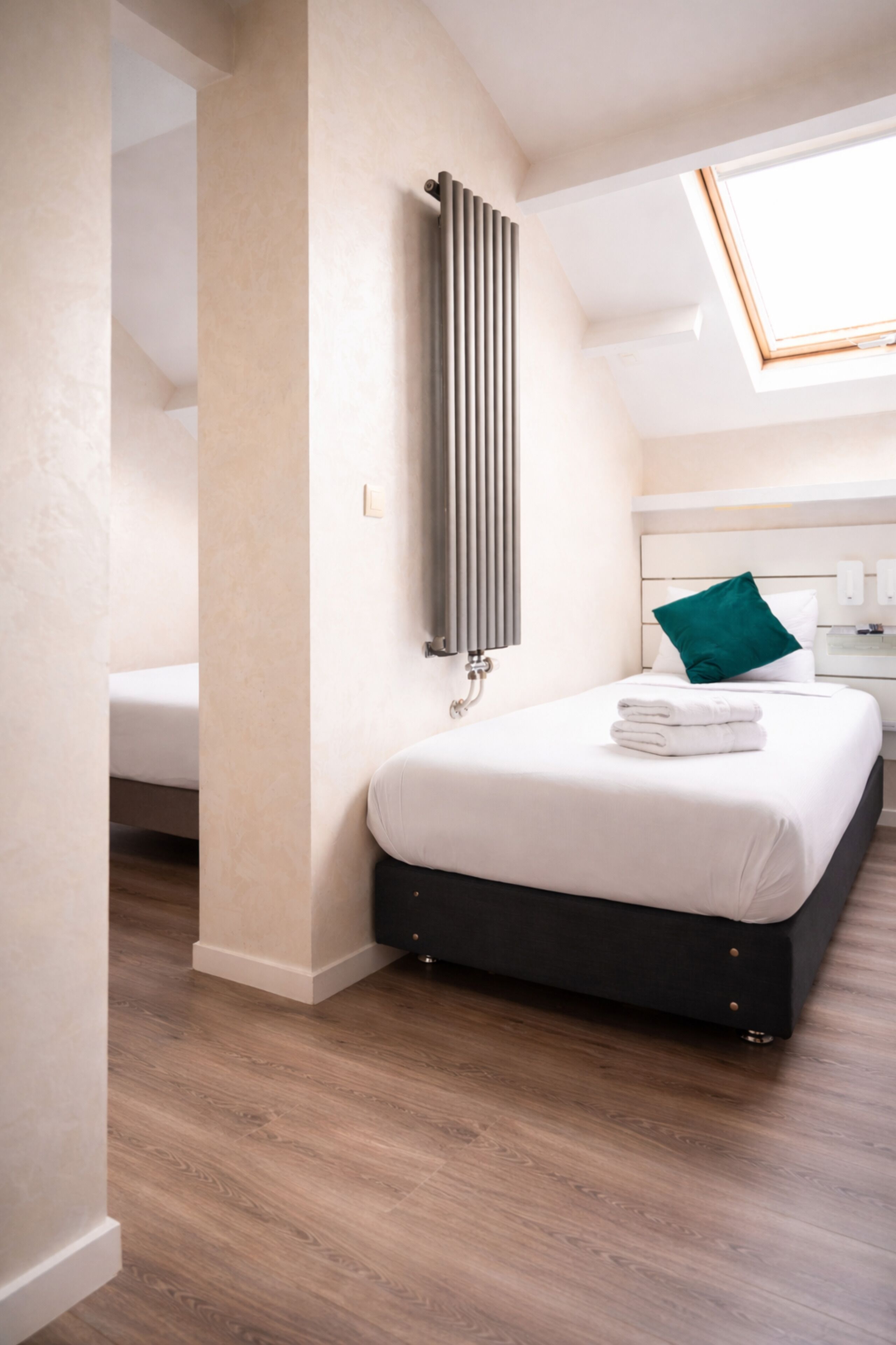 A modern bedroom with a skylight, a radiator, a bed with a green pillow, and a neatly made bed.