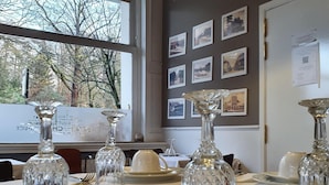 Een eettafel gedekt met witte borden, kommen en bestek, met kristalglaswerk en ingelijste foto's aan de muur.