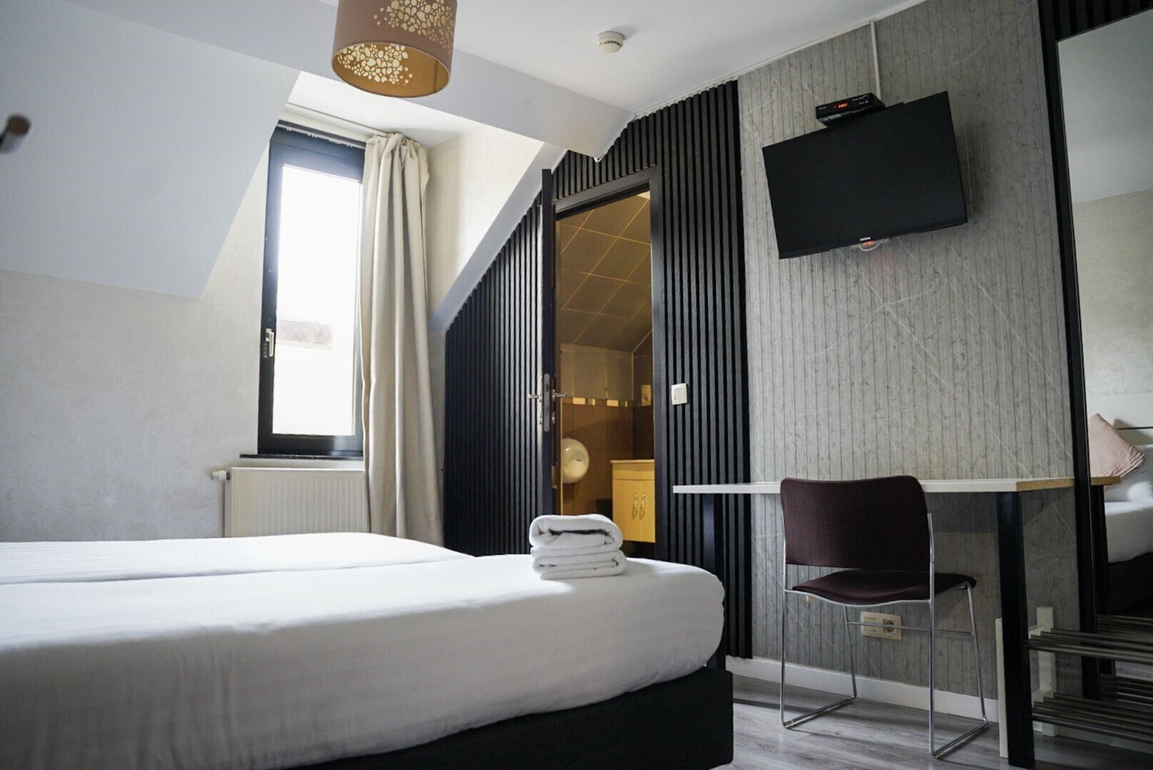 Une chambre d’hôtel avec un lit, un bureau, une chaise, une télévision et une fenêtre avec des rideaux.