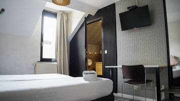 Une chambre d’hôtel avec un lit, un bureau, une chaise, une télévision et une fenêtre avec des rideaux.