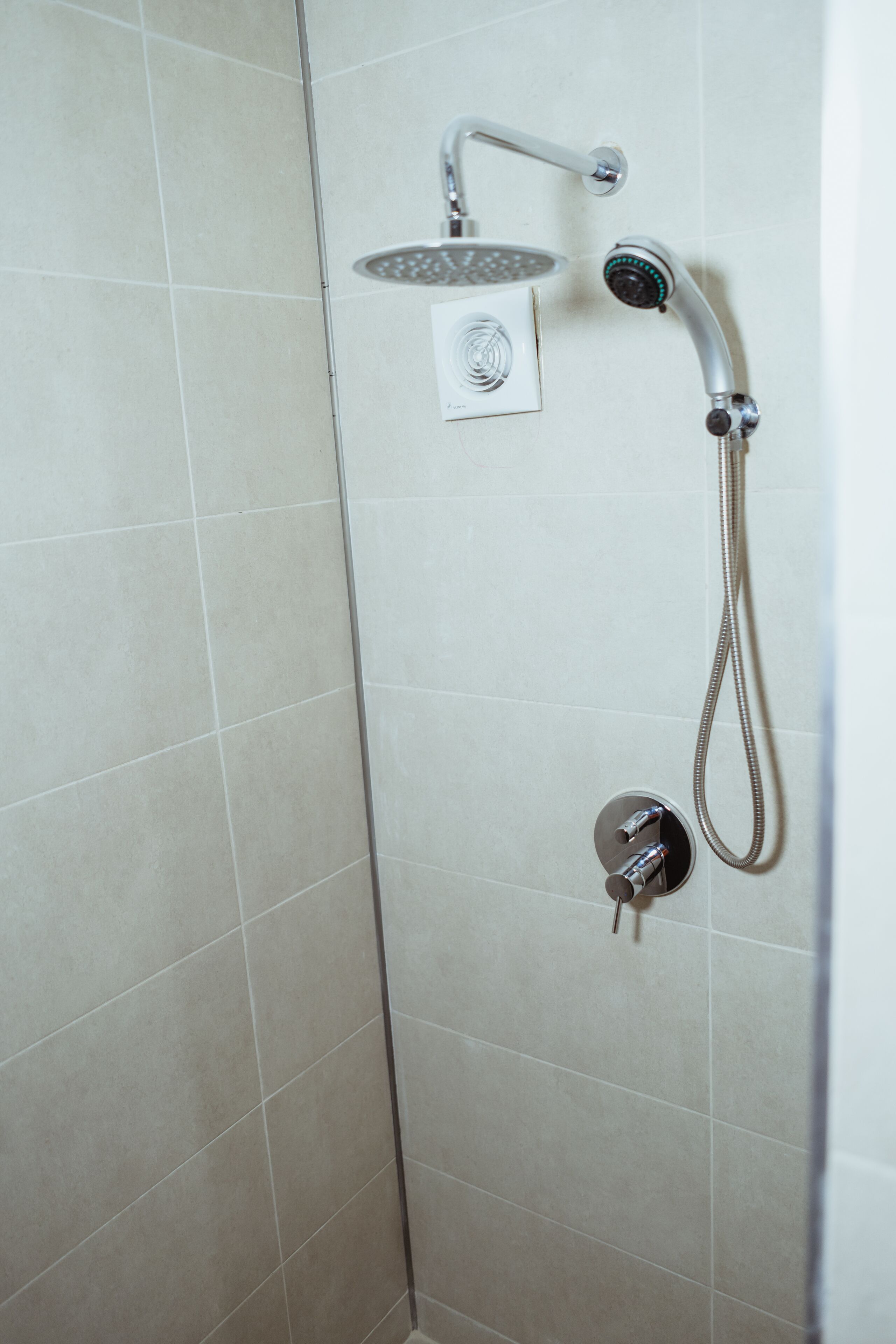 A shower with a handheld showerhead and a fixed showerhead, both mounted on a tiled wall.