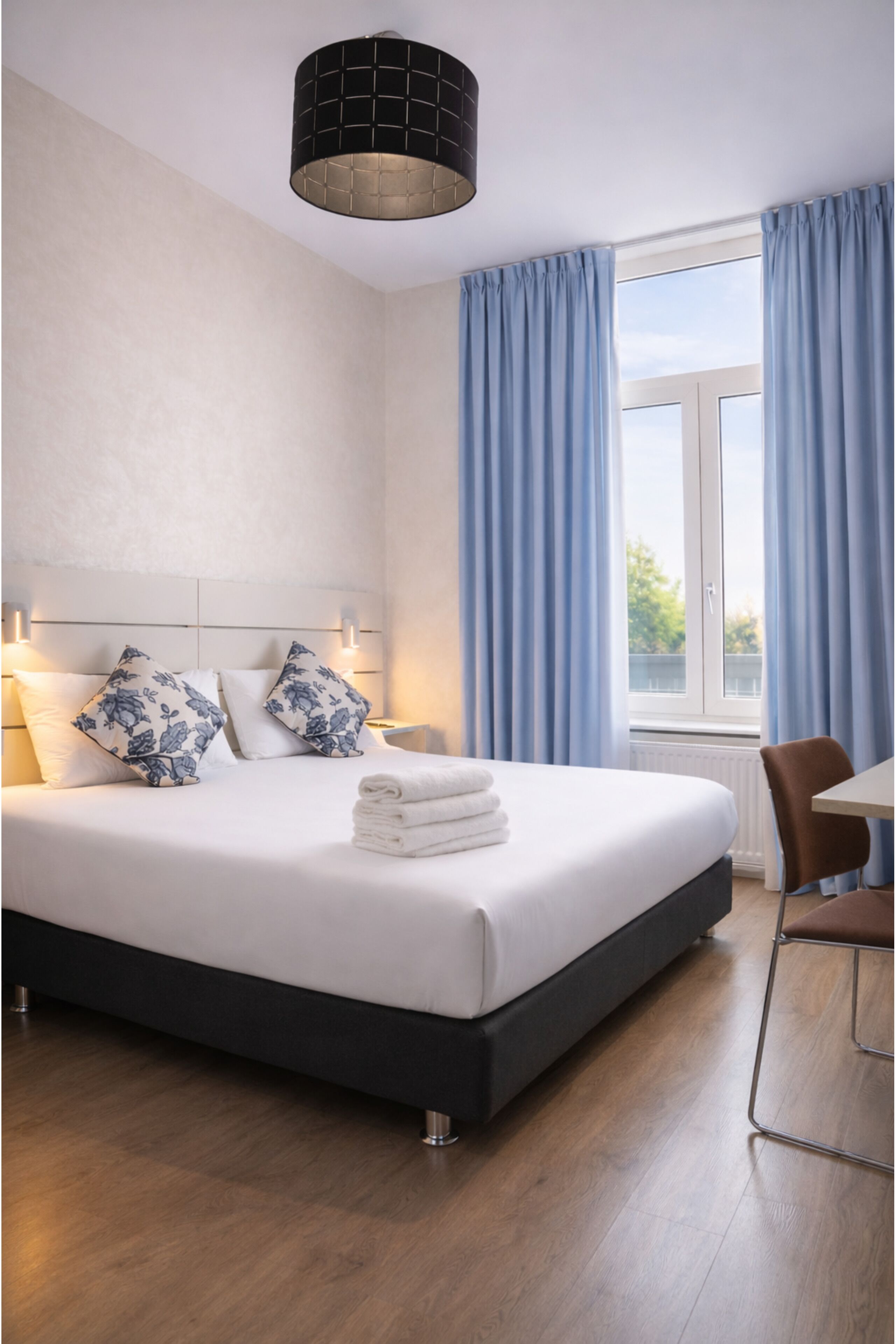A modern hotel room with a large bed, a desk, and a window with curtains.